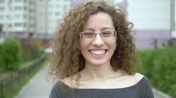 Beautiful smiling woman in glasses with curly hair walks on a city street. — Stock Photo, Image