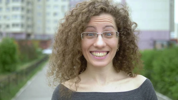 Mooie glimlachende vrouw in bril met krullend haar wandelingen op een stad straat. — Stockfoto