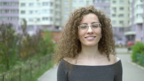 街の通りを歩く巻き毛のメガネの美しい笑顔の女性. — ストック動画