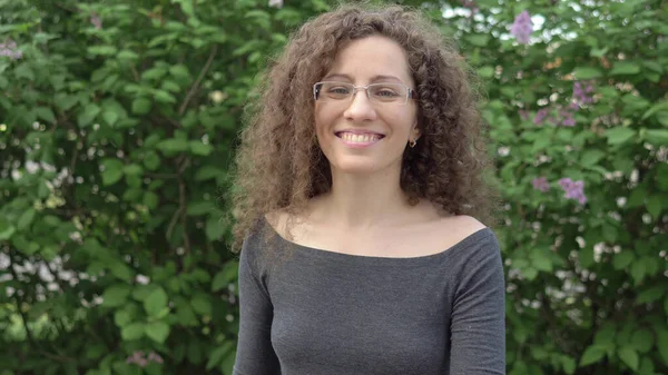 Hermosa chica en gafas con pelo rizado paseos en el parque sobre un fondo de árboles —  Fotos de Stock