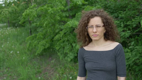 Girl in glasses with curly hair walks in the park on a background of trees — Stock Photo, Image