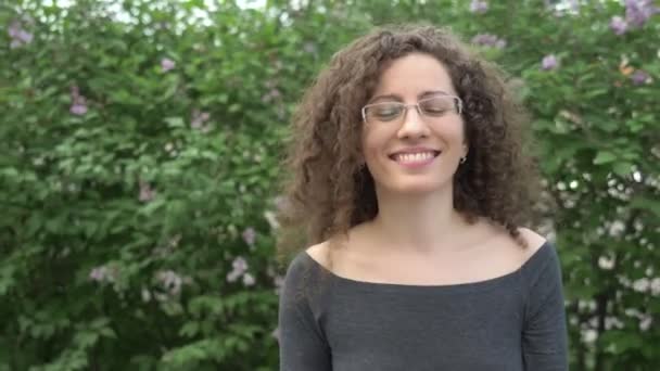 Chica en gafas con pelo rizado camina en el parque sobre un fondo de árboles — Vídeo de stock