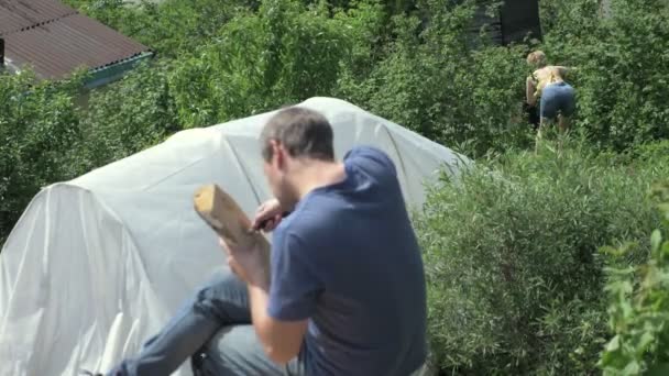 Лисий мушоподібний чоловік вирізає отвір в дерев'яній дошці з ножем на відкритому повітрі — стокове відео