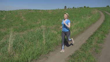 Tam yükseklik. Açık bir yaz gününde spor giysili bir kadın sahada koşar.