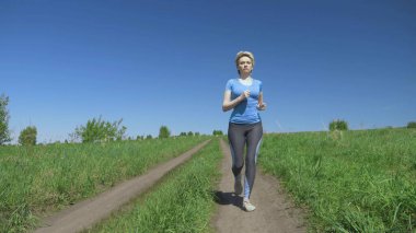 Tam yükseklik. Açık bir yaz gününde spor giysili bir kadın sahada koşar.