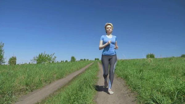 Tam yükseklik. Açık bir yaz gününde spor giysili bir kadın sahada koşar.