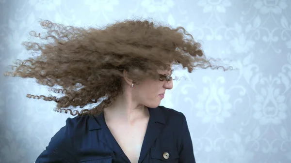 Kıvırcık saçlı, gözlüklü kadın başını çeviriyor, saçlarında rüzgar var. — Stok fotoğraf