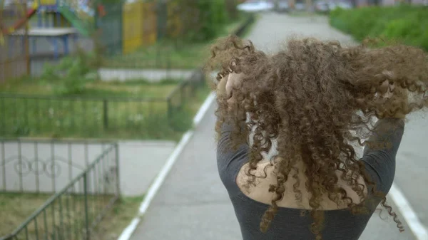 Вид сзади. Женщина с вьющимися волосами касается волос, стоящих на городской улице. — стоковое фото