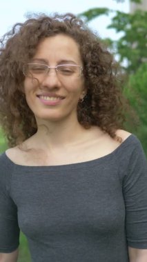 Dikey. Kıvırcık saçlı gözlüklü kız parkta yürüyor.