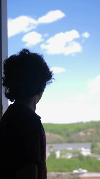 Verticalmente. silhueta. adolescente senta-se em uma janela contra um céu azul — Fotografia de Stock