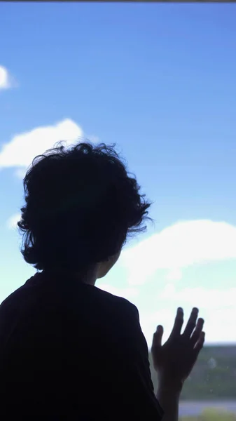 Вертикально. Силуэт. teenager sits on a window sill against a blue sky — стоковое фото