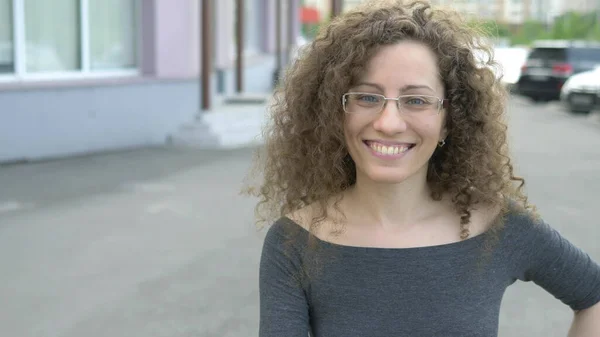 Beautiful girl in glasses with curly hair walks in the park on a background of trees — Stock Photo, Image