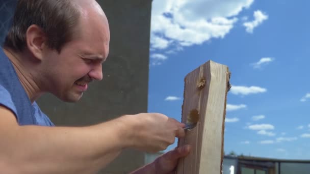 Een dorpeling, een kale man kerft patronen met een mes op een houten plank — Stockvideo