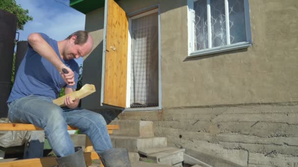 Деревенский житель, лысый мужчина вырезает узоры с ножом на деревянной доске — стоковое видео