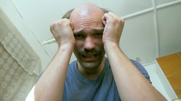 Careca homem bigode expressa tristeza enquanto sentado em uma pobre sala de desmoronamento — Vídeo de Stock
