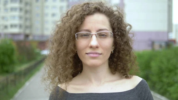 beautiful smiling woman in glasses with curly hair walks on a city street.