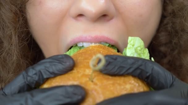 Primer plano de los labios. mujer come una jugosa hamburguesa, manos en guantes de goma negro — Vídeo de stock