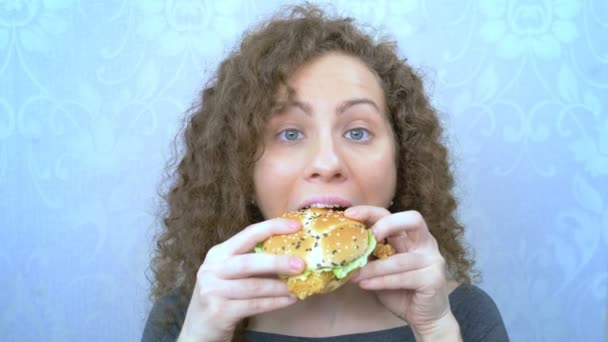 Bella donna con i capelli ricci mangia un hamburger succoso. primo piano — Video Stock
