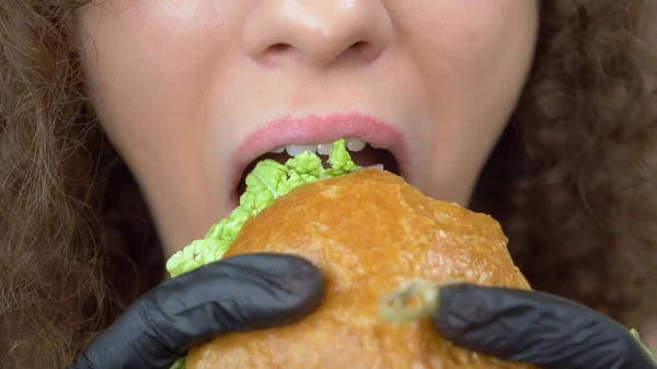 closeup of the lips. woman eats a juicy hamburger, hands in black rubber gloves