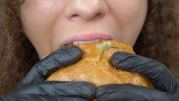 Närbild av läpparna. kvinna äter en saftig hamburgare, händer i svart gummi handskar — Stockvideo