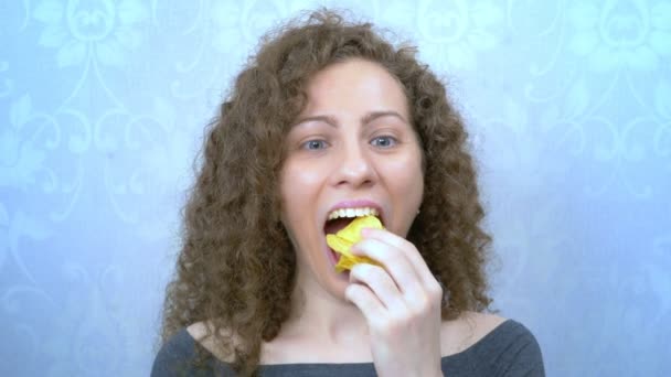 Красивая кудрявая девушка с удовольствием ест картофельные чипсы. портрет — стоковое видео