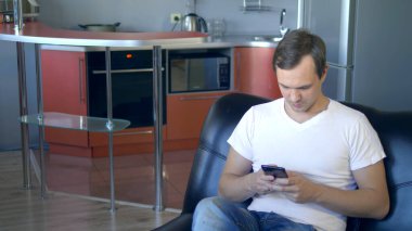 Sinirli adam telefonu fırlatıyor. Oturma odasının mutfağında bir koltukta oturuyor.