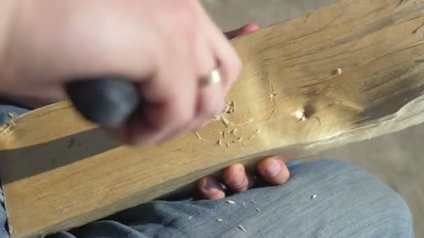 Man snijdt een gat in een houten plank met een mes buiten — Stockvideo