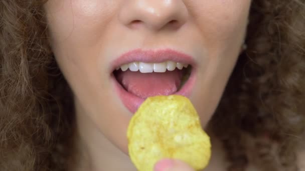 Крупный план губ. красивая кудрявая девушка с удовольствием ест чипсы — стоковое видео