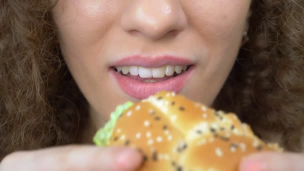 Schöne Frau mit lockigem Haar isst einen saftigen Hamburger. Nahaufnahme — Stockvideo