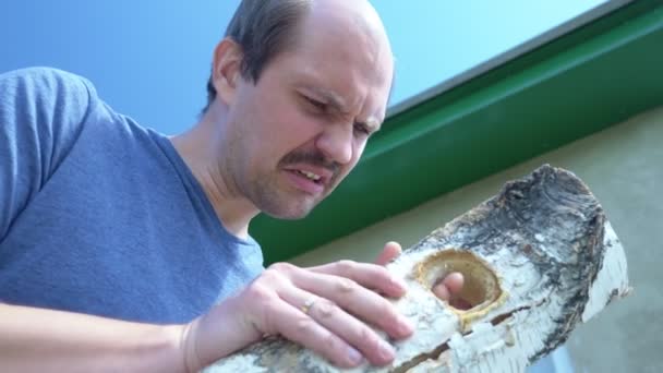 Careca homem bigode corta um buraco em uma placa de madeira com uma faca ao ar livre — Vídeo de Stock