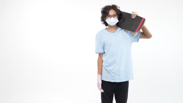 Isolerad vit bakgrund. pojke i handskar och en medicinsk mask med en skateboard — Stockvideo