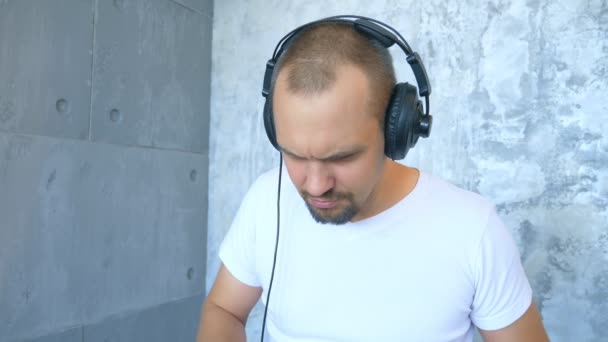 Ein Mann mit Kopfhörer schreibt elektronische Musik mit Midi-Tastatur und Laptop — Stockvideo