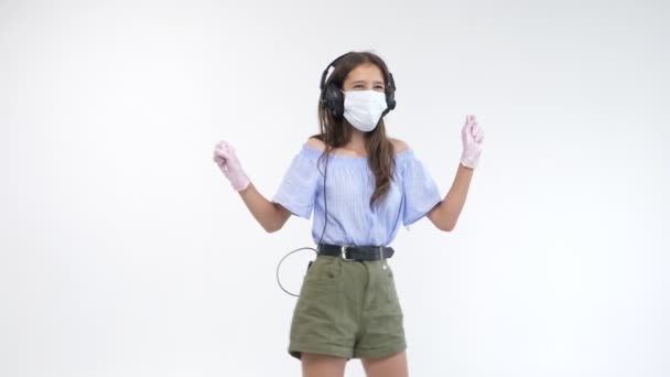 Geïsoleerde witte achtergrond. meisje in handschoenen en een masker in hoofdtelefoon danst — Stockvideo