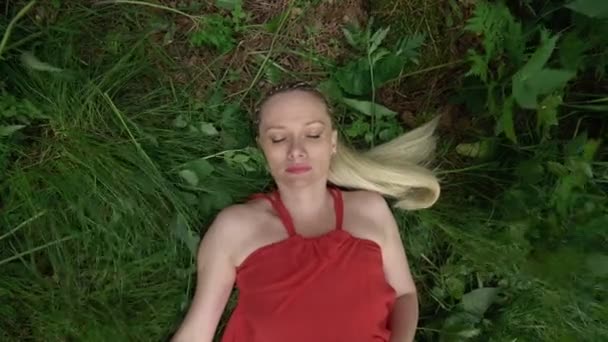Una mujer yace en la hierba en el viento inconsciente, abre sus ojos con miedo — Vídeos de Stock