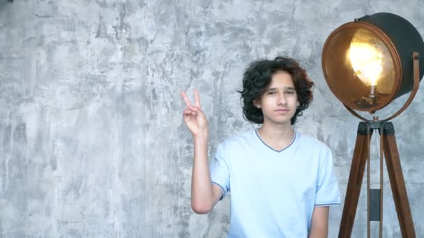 Bonito teen menino com curly cabelo mostra dois dedos gesto — Vídeo de Stock
