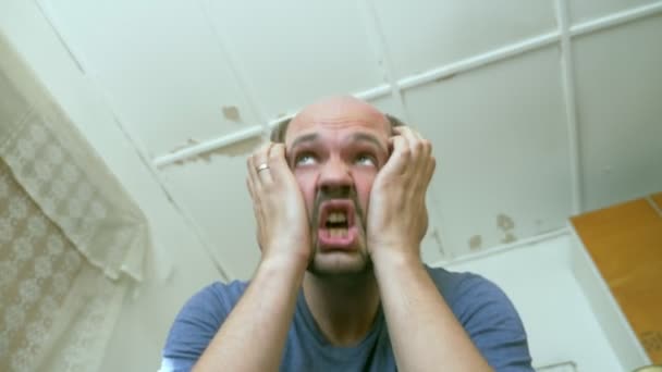 Careca homem bigode expressa tristeza enquanto sentado em uma pobre sala de desmoronamento — Vídeo de Stock
