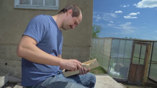 Деревенский житель, лысый мужчина вырезает узоры с ножом на деревянной доске — стоковое видео