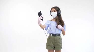 Beyaz arka plan. Eldivenli kız ve kulaklıklı tıbbi maske selfie yapıyor.