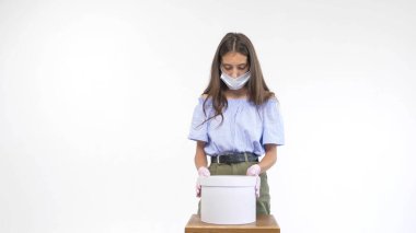 Eldiven giymiş güzel bir kız ve tıbbi bir maske hediye kutusunu açıyor.