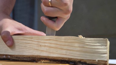 Adam dışarıda bıçakla tahta bir tahtada delik açıyor.