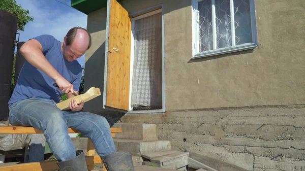 Hombre hace un agujero en una tabla de madera con un cuchillo al aire libre — Foto de Stock