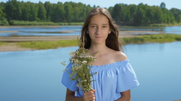 Дівчина з довгим волоссям дивиться в камеру на фоні річки — стокове відео