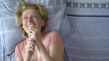 Hamilelik testi sonuçlarına bakan mutlu yetişkin kadın yatakta yatarken seviniyor.