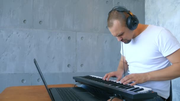 En man i hörlurar skriver elektronisk musik med ett midi-tangentbord och bärbar dator — Stockvideo