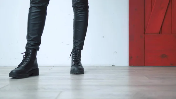 Primer plano. piernas femeninas en cuero negro flaco y botas sobre un fondo rojo blanco — Foto de Stock
