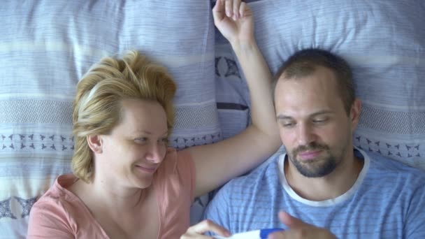 Пара чоловік і жінка, які спостерігають за результатами тесту на вагітність, лежать у ліжку — стокове відео