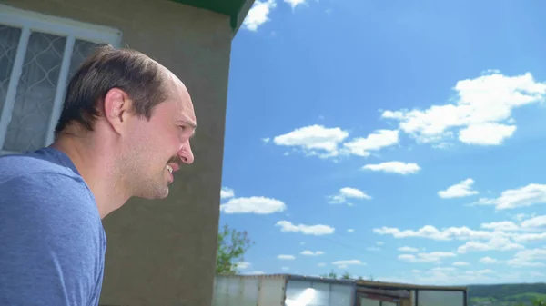 Primer plano, hombre calvo bigotudo al aire libre contra un cielo azul y una casa de pueblo —  Fotos de Stock