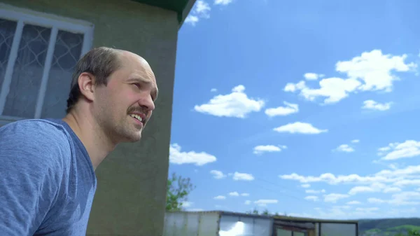 Primer plano, hombre calvo bigotudo al aire libre contra un cielo azul y una casa de pueblo — Foto de Stock
