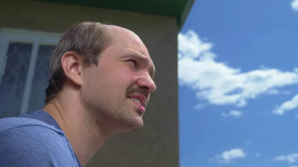 Primer plano, hombre calvo bigotudo al aire libre contra un cielo azul y una casa de pueblo — Foto de Stock