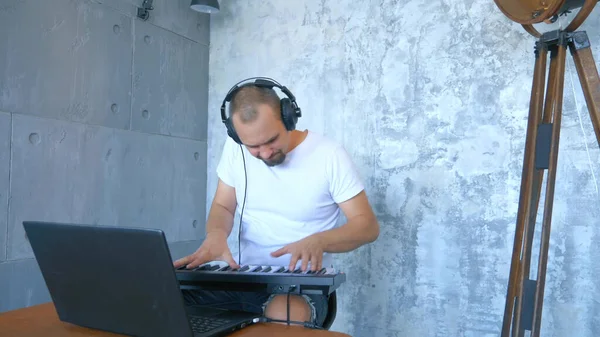 Мужчина в наушниках пишет электронную музыку с клавиатуры и ноутбука — стоковое фото